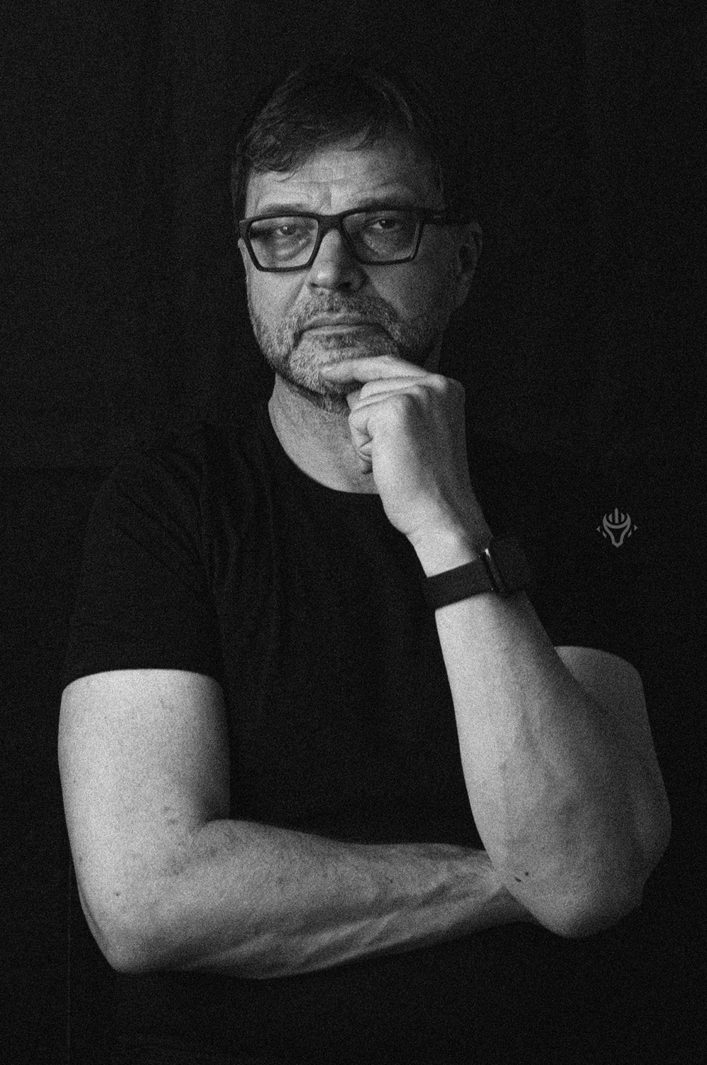 Czarno-biały portret mężczyzny w okularach, z dłonią pod brodą.