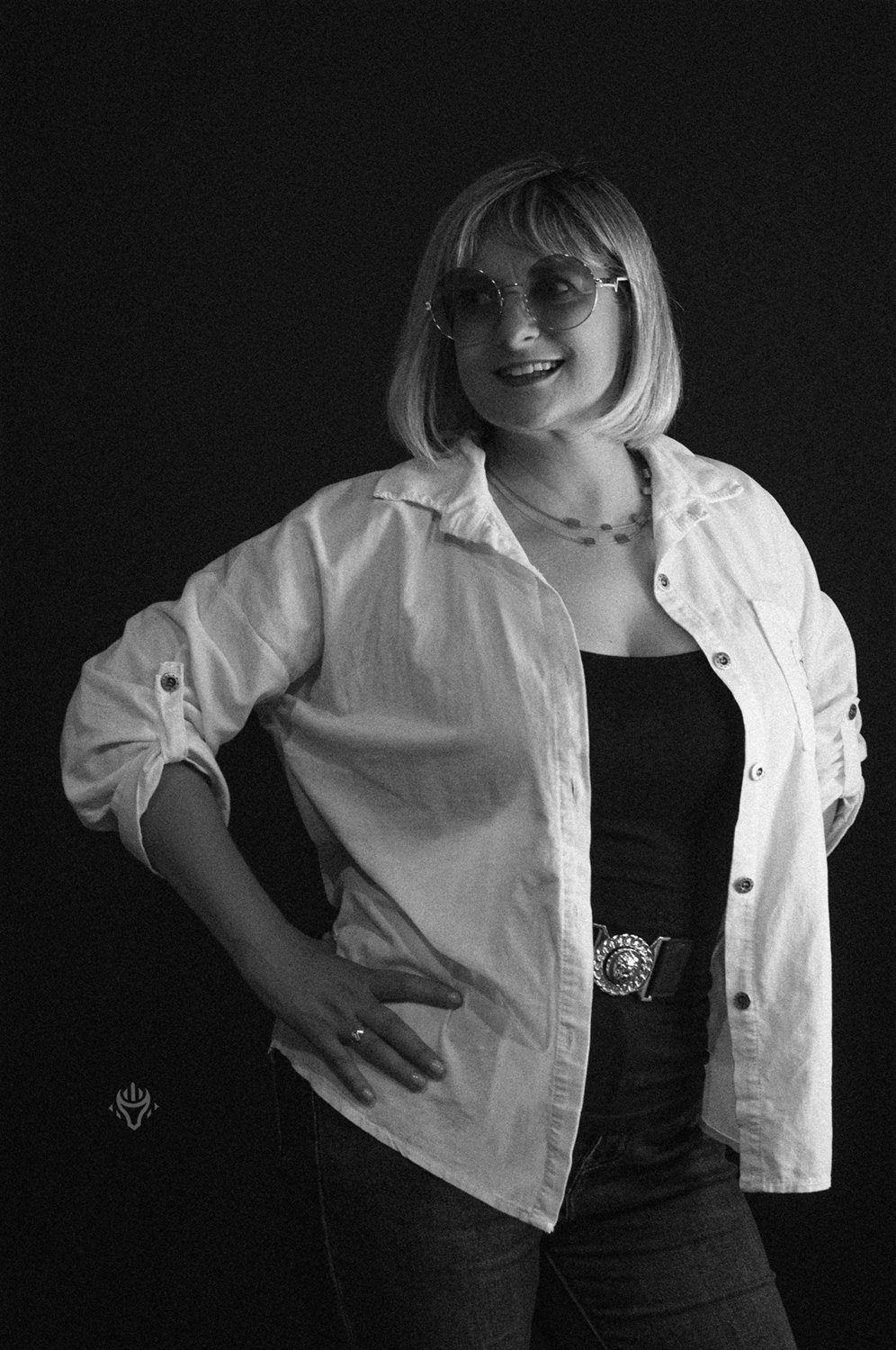 Czarno-biały portret kobiety w jasnej koszuli, z dłonią na biodrze.