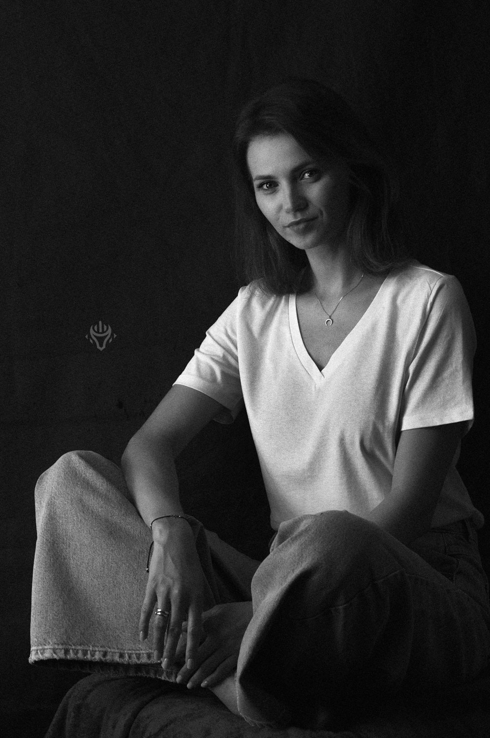 Czarno-biały portret kobiety w jasnym t-shircie na ciemnym tle.